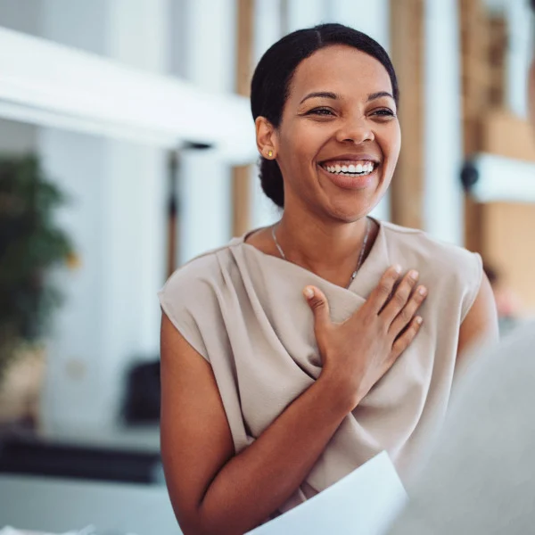 Smiling woman with hand on chest talks to another person indoors.